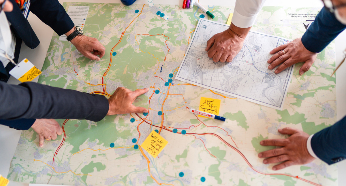 Eine Straßenkarte liegt auf einem Tisch. Menschen beugen sich über die Karte.