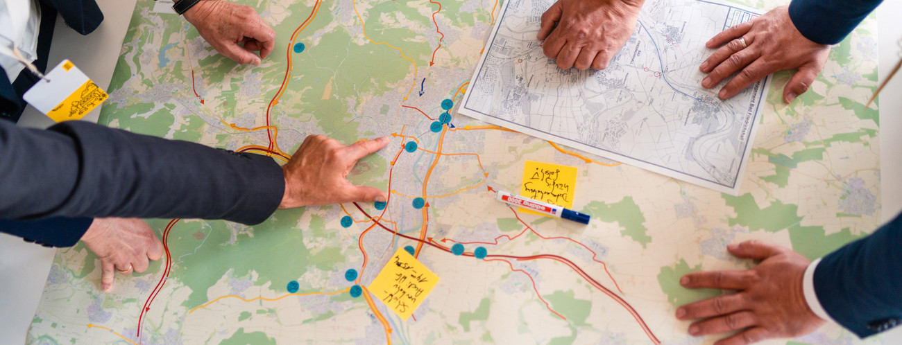 Eine Straßenkarte liegt auf einem Tisch. Menschen beugen sich über die Karte.