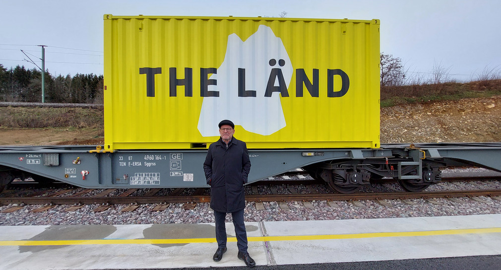 Minister Hermann steht vor einem Container im THE-LÄND-Design.