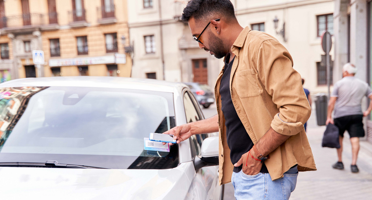 Mann in der Stadt mietet ein Gemeinschaftsauto über eine mobile Anwendung, indem er einen QR-Code scannt.