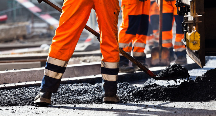 Arbeiter in Warnwesten arbeiten mit Schaufeln auf einer Baustelle an einer Straße.