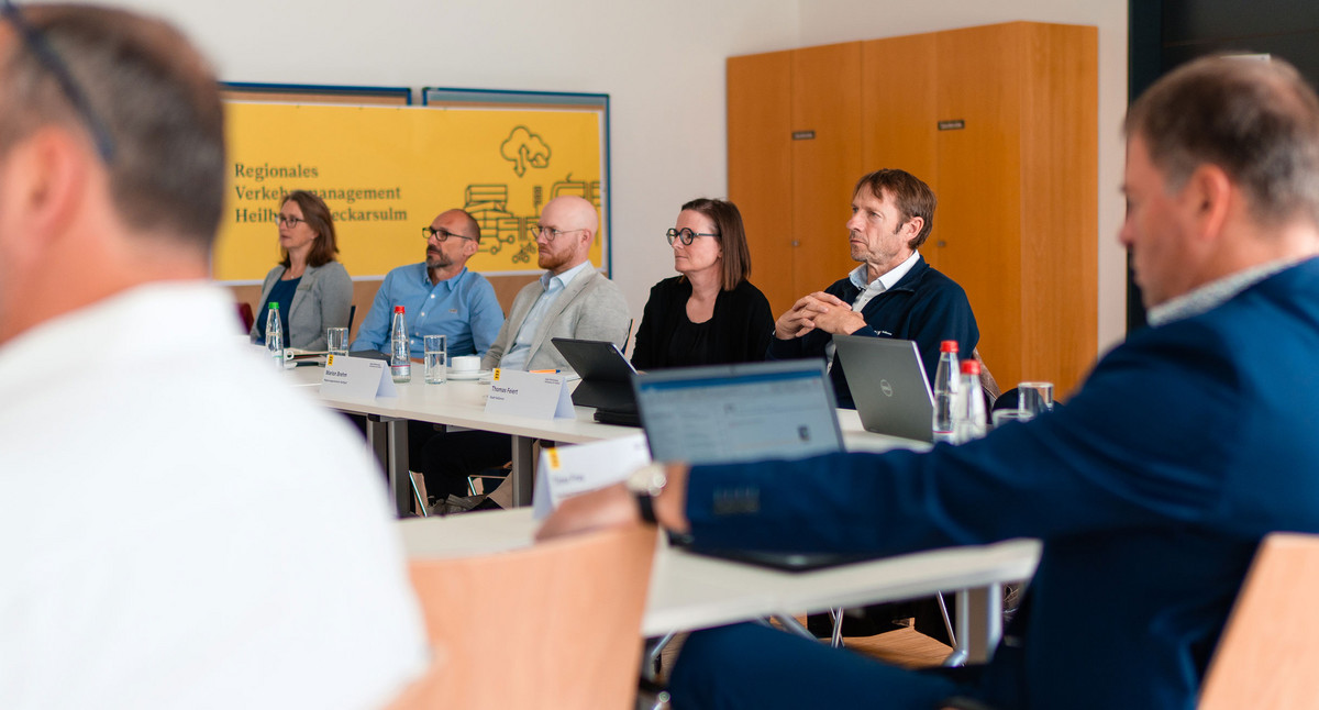 Menschen sitzen an Tischen und hören einer Präsentation zu.