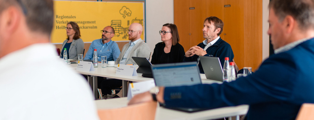 Menschen sitzen an Tischen und hören einer Präsentation zu.