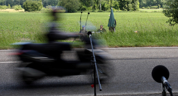 Ein Motorradfahrer fährt an aufgestellten Mikrofonen zur Lärmmessung am Straßenrand vorbei (Bild: LUBW)