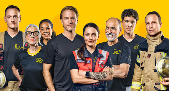 Rettungskräfte und der ehemalige VfB-Torwart Timo Hildebrand unterstützen 2024 das Team Vision Zero. In diesem Bild steht das ganze Team in Team Vision Zero-Shirt oder Uniform vor gelbem Hintergrund.