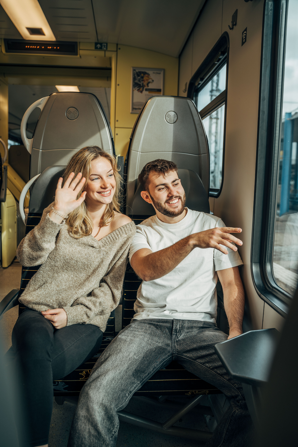 Ein junger Mann und eine junge Frau im bwegt-Zug winken aus dem Fenster.