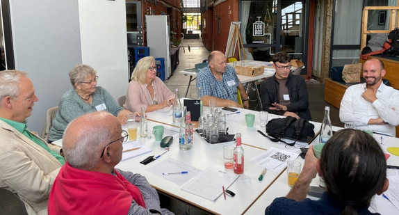 Mehrere Menschen sitzen an einem Gruppentisch und diskutieren.