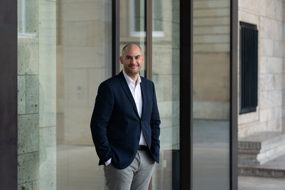 Porträtbilder Minister Dr. Danyal Bayaz Finanzminister Danyal Bayaz steht vor dem Kunstgebäude am Schlossplatz in Stuttgart, angelehnt an eine Glasfassade, die Details der Gebäudestruktur widerspiegelt.