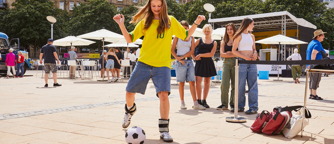 Mädchen mit gelbem T-Shirt spielt Fußball mit Gewichten an den Füßen.