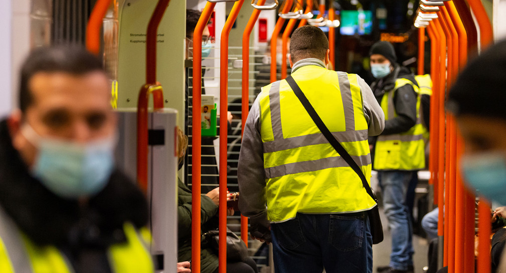 Mehrere Männer in gelben Warnwesten kontrollieren in einer U-Bahn die Einhaltung der 3G-Regeln.