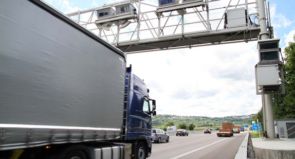 Mehrspurige Autobahn über die eine Brücke mit aufgehängtem technischen Geräten führt.