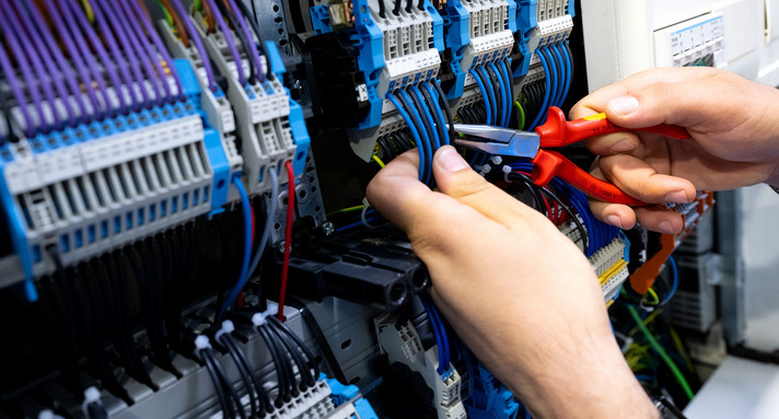 Ein Elektriker arbeitet an einem Schaltschrank mit einer Zange.