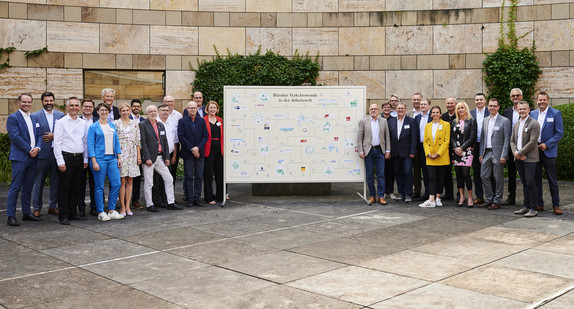 Gruppenbild des Bündnisses. In der Mitte steht eine Tafel mit den verschiedenen Logos der Firmen. 