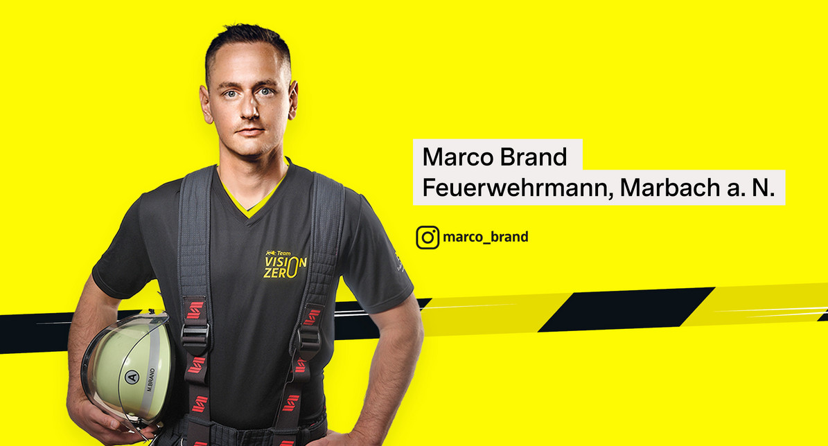Porträtfoto von Feuerwehrmann Marco Brand. Er trägt ein Team Vision Zero-Shirt und hält einen Feuerwehrhelm unter dem Arm.