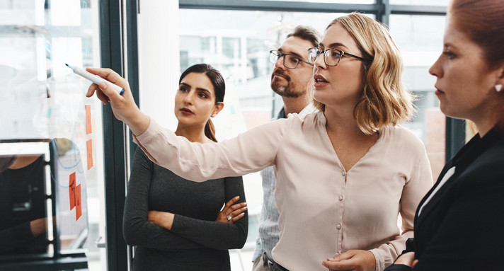 Frau, Gruppe und Zusammenarbeit mit Notizen an der Tafel mit Überprüfung, Zuhören und Planen mit Brainstorming. Coach, Training und Team durch Glaswand, Fragen und Diskussion mit Strategie im Büro