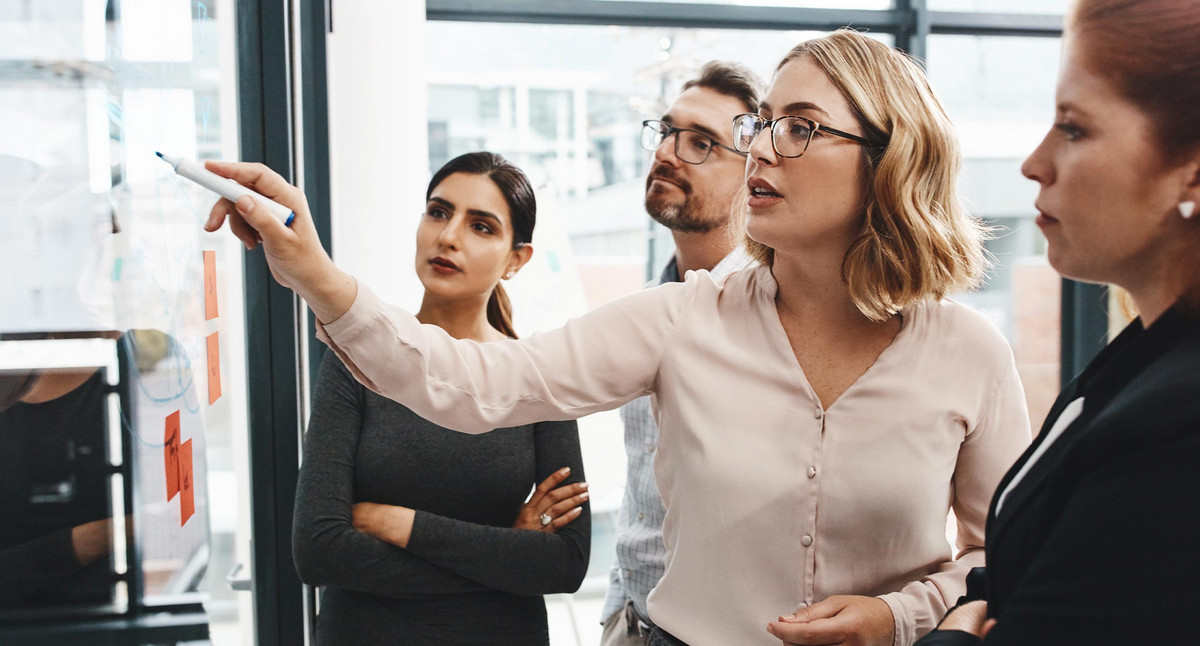 Frau, Gruppe und Zusammenarbeit mit Notizen an der Tafel mit Überprüfung, Zuhören und Planen mit Brainstorming. Coach, Training und Team durch Glaswand, Fragen und Diskussion mit Strategie im Büro