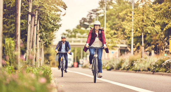 Zwei Radfahrende fahren auf einem Radweg am Straßenrand.