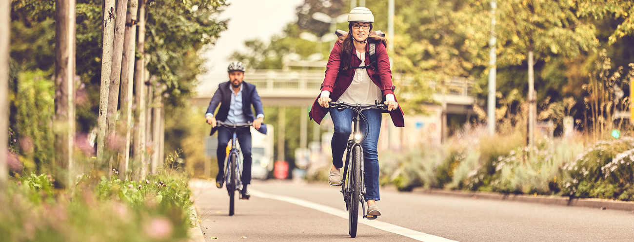 Zwei Radfahrende fahren auf einem Radweg am Straßenrand.