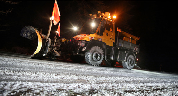 Ein Fahrzeug des Winterdienst räumt Schnee und streut Salz auf einer Straße im Dunkeln.