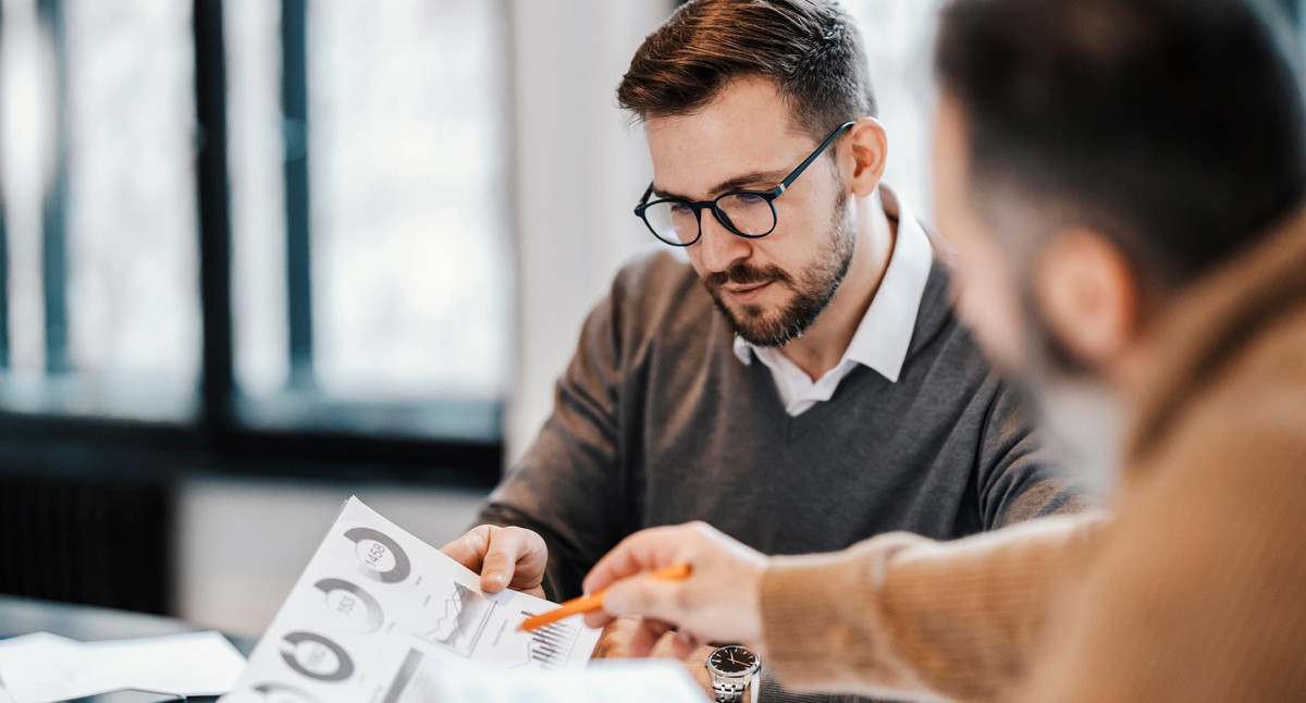 Zwei Kollegen sitzen im Besprechungsraum und diskutieren Diagramme und Statistiken.
