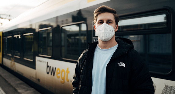 Ein Mann mit FFP2-Maske steht vor einem Zug am Bahnhof