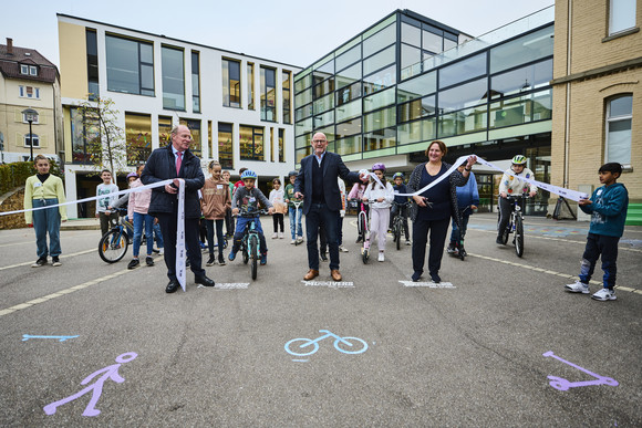 Verkehrssicherheit MOVERS – Aktiv zur Schule Minister Hermann, Ministerin Schopper und Innenstaatssekretär Klenk beim Startschuss von MOVERS, während sie das Band durchschneiden. Im Hintergrund Kinder zu Fuß, mit dem Fahrrad oder Roller.