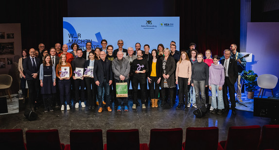 Mehrere Menschen stehen auf einer Bühne zu einem Gruppenbild zusammen.