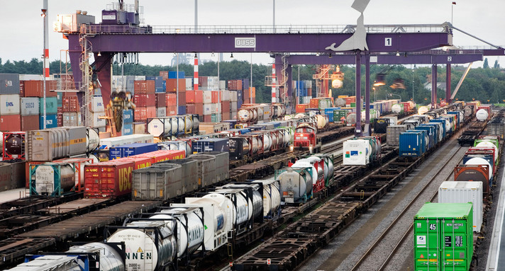 Container werden auf Zugwaagons verladen, die auf mehreren Gleisen stehen.