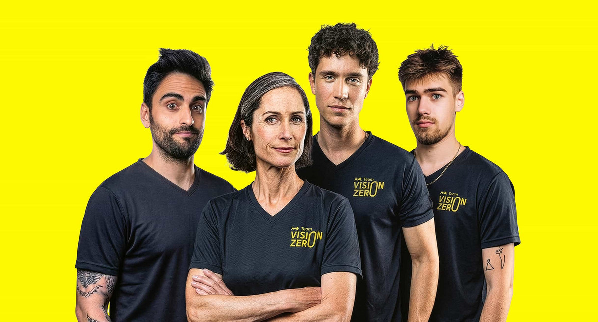 Gruppenbild von vier Personen. Drei junge Männer, in ihrer Mitte eine Frau mittleren Alters, die die Mutterfigur darstellt. Alle stehen nebeneinander, blicken frontal in die Kamera und tragen dabei ein Team Vision Zero-Shirt.