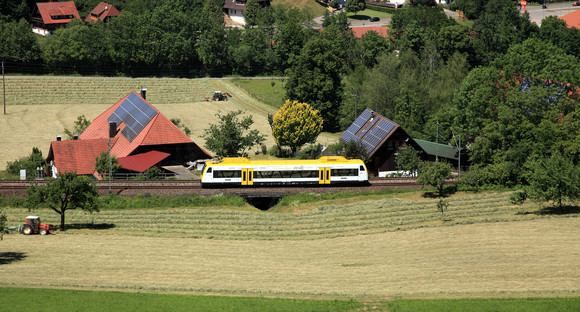 Gelb-weißer Zug der Ortenau-S-Bahn fährt entlang einer Bahnstrecke.