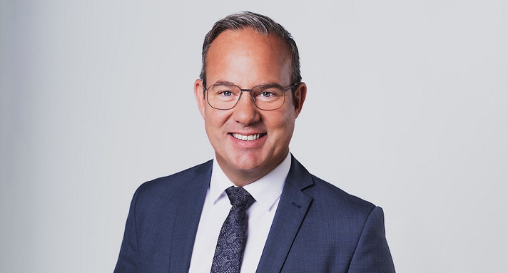Ein Mann im Anzug lacht in die Kamera.