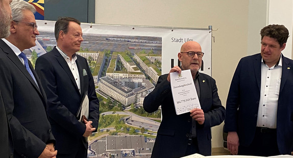 Minister Hermann hält den Zuwwndungsbescheid in Höhe von 104.779.545 Euro in die Kamera. Nebenihm stehen Regierungspräsident Tappeser, Oberbürgermeister Czisch und andere.