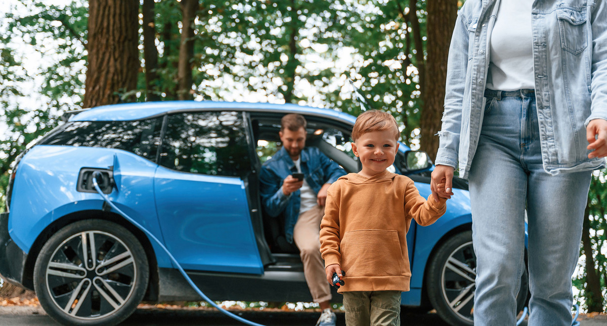 Ein Kind und eine Mutter laufen von einem E-Auto weg in dem noch der Vater sitzt.