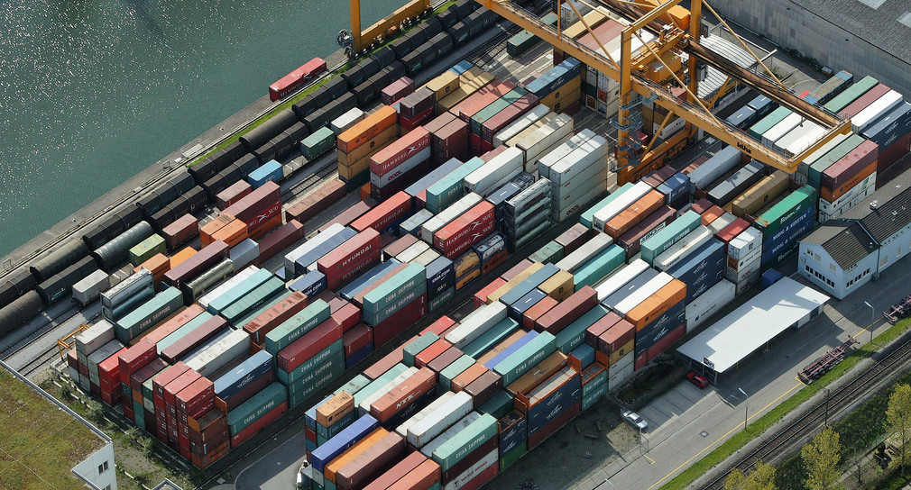 Große Hafenfläche am Ufer eines Flusses ist vollgestellt mit Containern. Zeigt Containerhafen Weil am Rhein.
