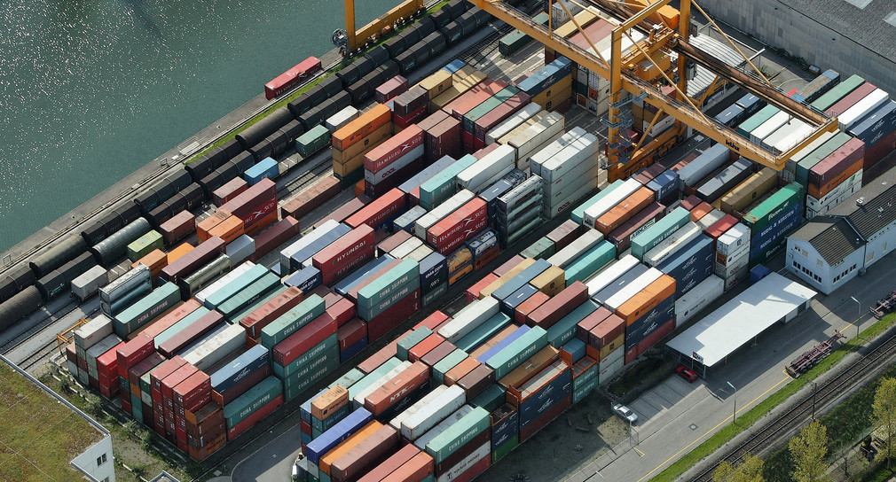 Große Hafenfläche am Ufer eines Flusses ist vollgestellt mit Containern. Zeigt Containerhafen Weil am Rhein.