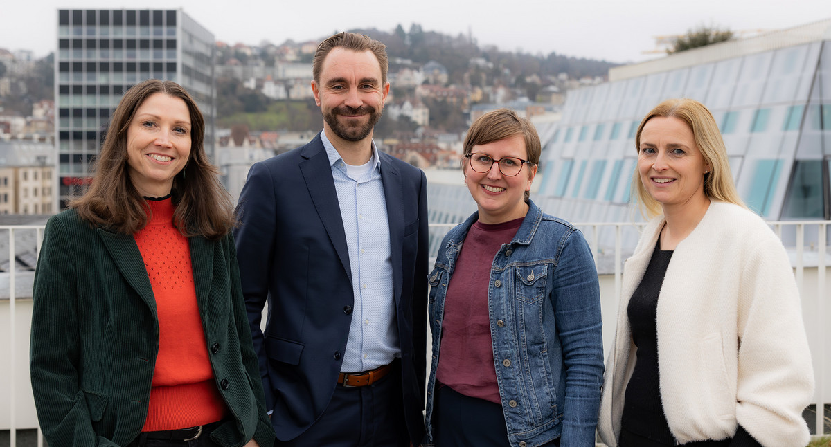 Drei Frauen und ein Mann stehen auf einer Dachterrasse mit Stuttgart im Hintergrund.