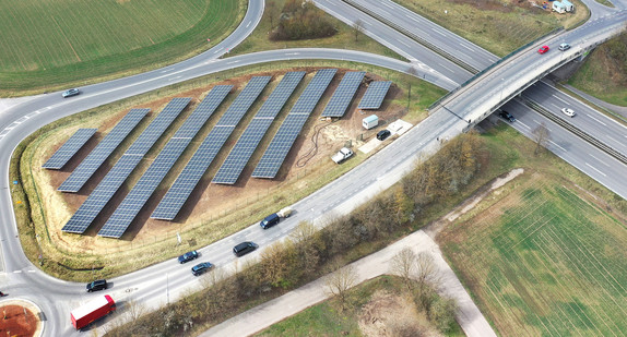 Viele Photovoltaikzellen stehen an einer Straße auf einer Wiese.