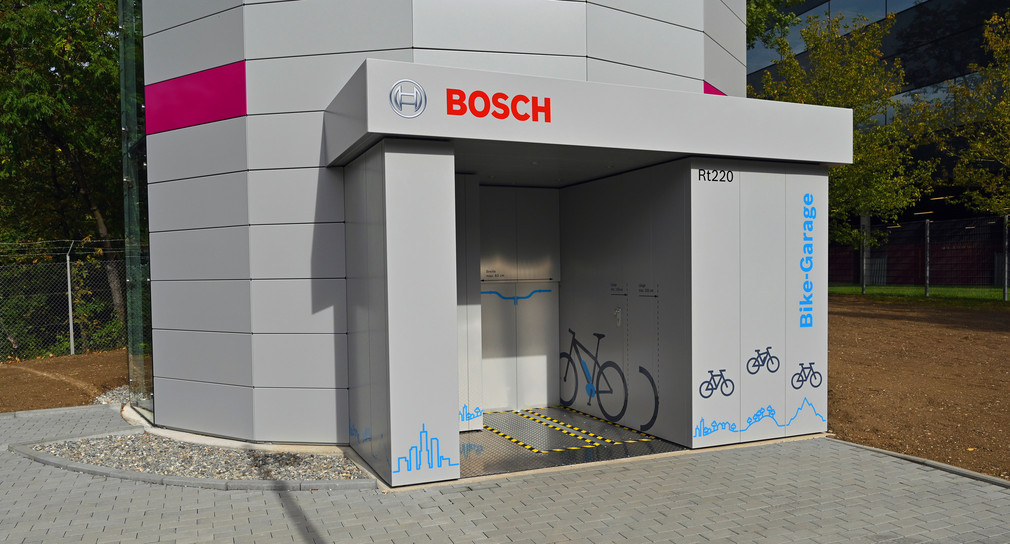 Fahrradgarage bei Bosch in Reutlingen. Gebäude mit bunten Kacheln verkleidet, steht auf einer grünen Wiese. Am Eingang hängen Aufkleber mit Fahrrädern drauf.