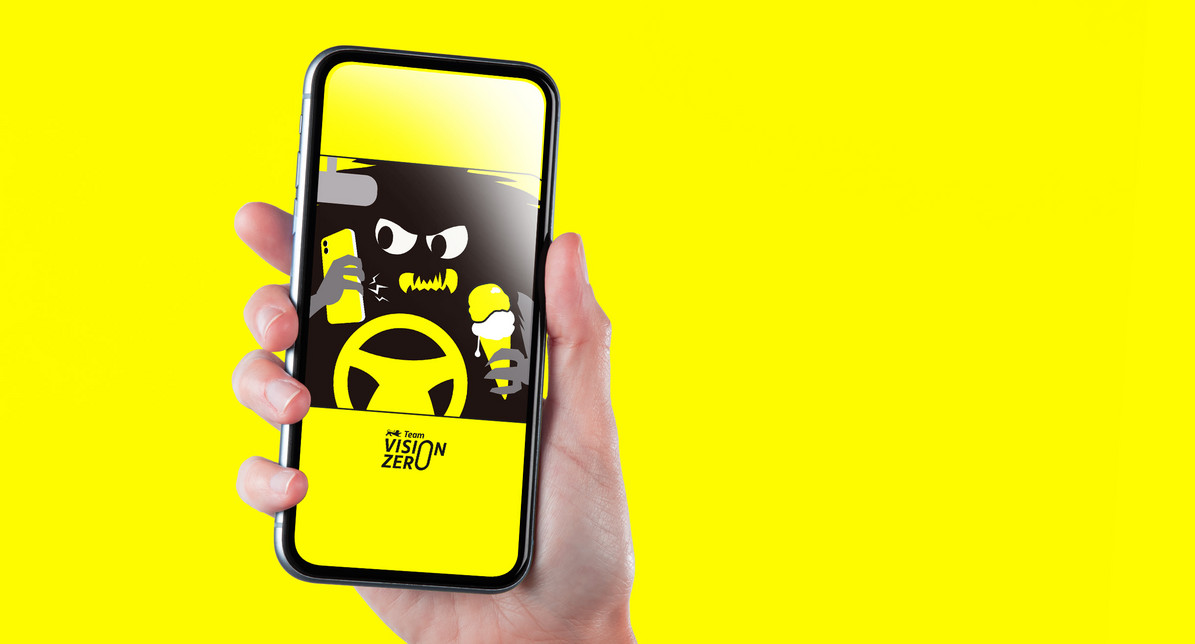 Eine Hand hält ein Smartphone ins Bild. Auf dem Bildschirm des Smartphones sieht man das Hintergrundbild, das man hier herunterladen kann. Das Hintergrundbild zeigt das Ablenkungsmonster am Steuer, mit Handy am Ohr und Eis in der Hand.