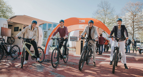 Mehrere Menschen stehen zum Losfahren bereit an Fahrrädern und E-Roller.