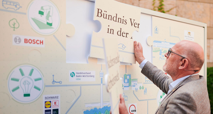 Ein Mann schiebt ein armbreites Puzzleteil an einer Wand an den richtigen Platz.