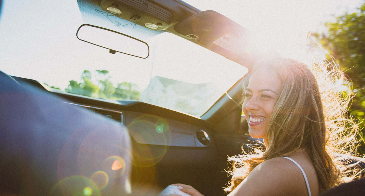 Frau sitzt lachend auf dem Beifahrersitz eines Cabrios