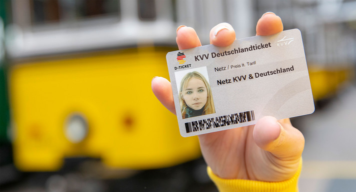 Ein Deutschlandticket wird von einer Person in die Kamera gehalten.