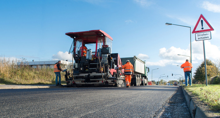 Bauarbeiter legen mit ihrer Teermaschine einen neuen Straßenbelag.