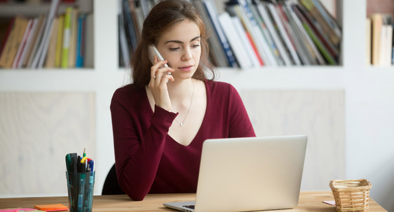 Eine Frau telefoniert und arbeitet am Laptop 