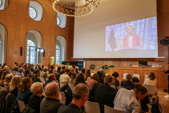 Zusammenhalt in der Transformation Tagung „Gemeinsam handeln“ Videobotschaft von Dr. Ursula von der Leyen, Präsidentin der Europäischen Kommission, auf der Leinwand vor den Tagungsteilnehmenden.