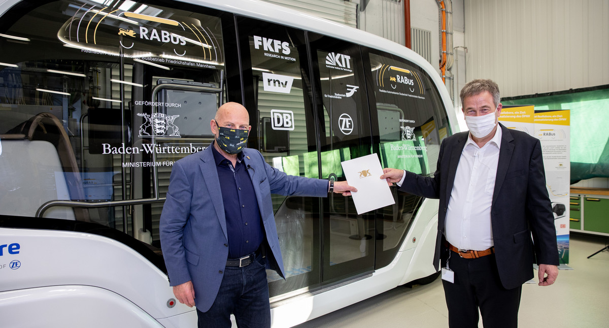 Verkehrsminister Winfried Hermann und Prof. Dr. Hans-Christian Reuss (FKFS) mit Übergabemappe vor dem autonomen Shuttlebus