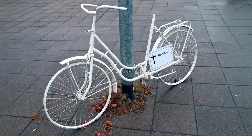 Ein weißes Fahrrad steht an einem Laternenmast.