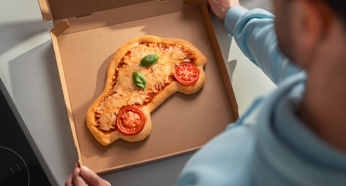 Blick über die Schulter eines Mannes. Er hält einen offenen Pizzakarton in den Händen. Darin befindet sich eine Pizza in der Form eines Autos.