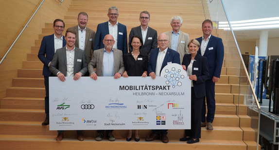 Verkehrsminister Hermann mit den Partnerinnen und Partnern des Mobilitätspaktes Heilbronn–Neckarsulm sowie einer Tafel mit den jeweiligen Unterschriften und Logos